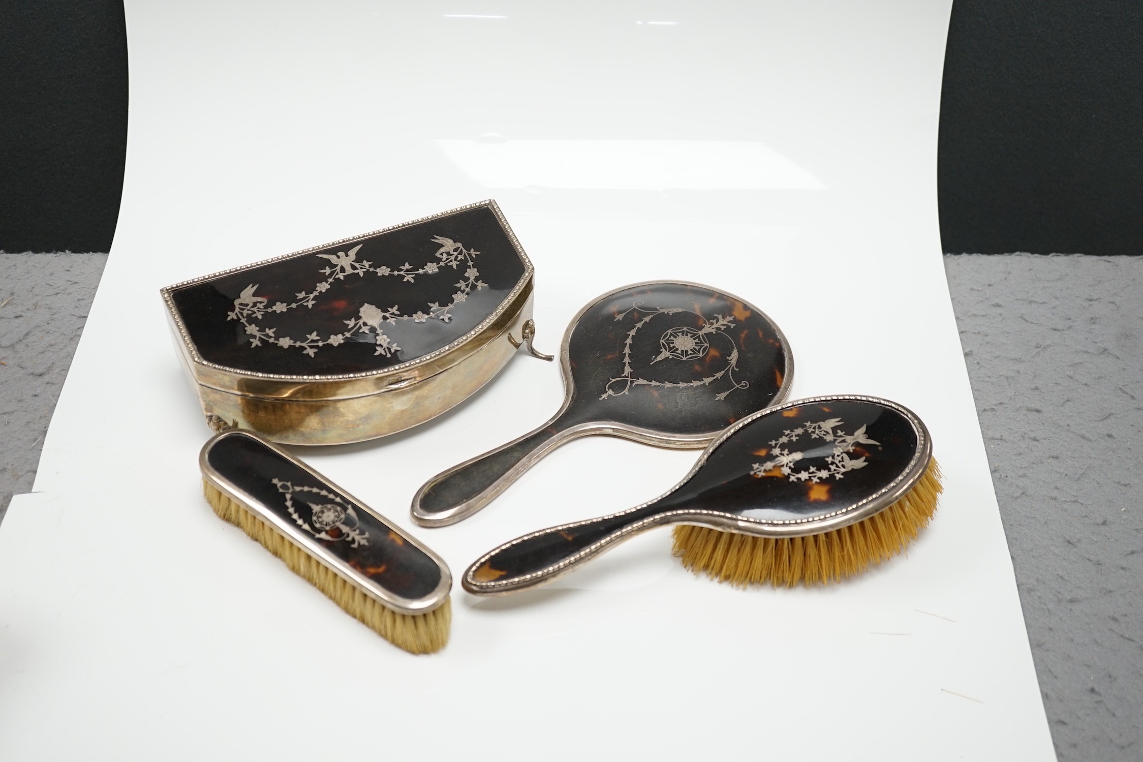 A George V silver and tortoiseshell piqué mounted trinket box, Levi & Salaman, Birmingham, 1918, 19cm and a matched three piece silver and tortoiseshell mounted mirror and brush set.
